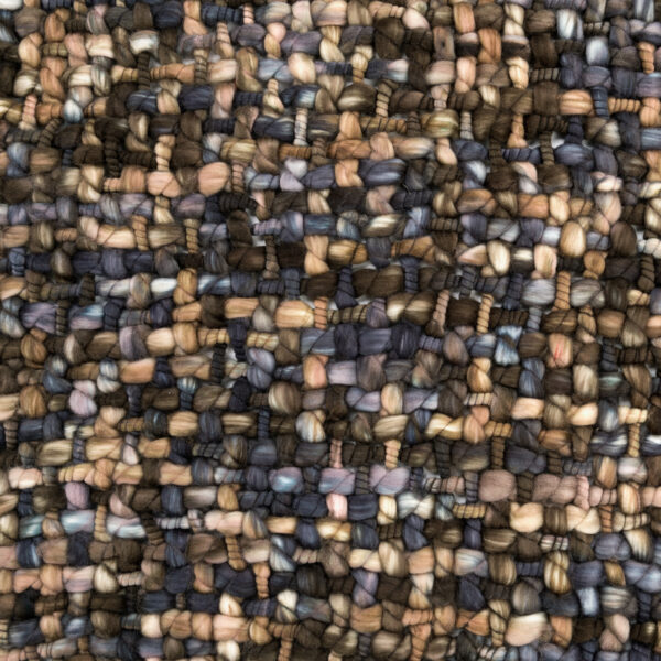 A close up view of the fabric of a black, brown, blue, and green woven throw blanket folded and tied with a cream bow and a tag.